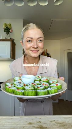 a woman holding a plate with cucumber sushi on it