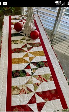 a christmas table runner with red and white ornaments on it, next to a small tree