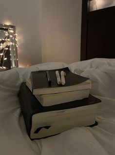 a stack of books sitting on top of a bed next to a mirror with lights in the background