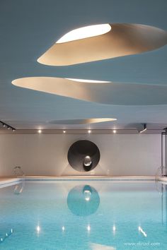 an indoor swimming pool with blue water and white lighting above it is illuminated by recessed lights