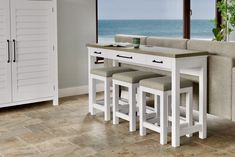 a kitchen table with four stools next to the ocean