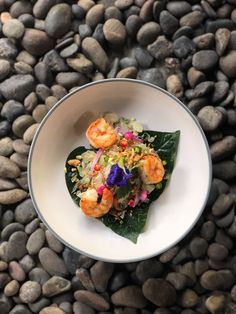 a white bowl filled with food sitting on top of a pile of rocks next to a green leaf