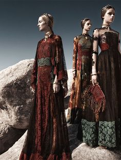 two women in long dresses standing next to each other near large rocks and boulders, both wearing headbands