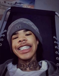 a young man with tattoos on his face sitting in a chair and smiling at the camera