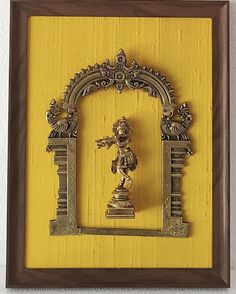 an ornate frame with a statue in the middle and a yellow wall behind it,