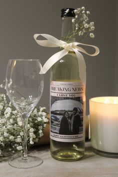 a bottle of wine next to a glass and candle on a table with white flowers