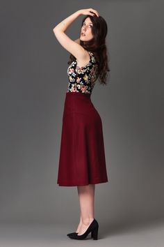 a woman in a floral top and maroon skirt poses for the camera with her hand on her head