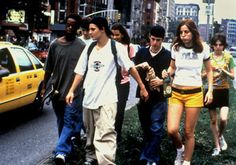 a group of young people walking down a street next to a yellow taxi and tall buildings