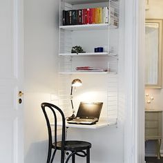 a laptop computer sitting on top of a desk next to a chair and bookshelf