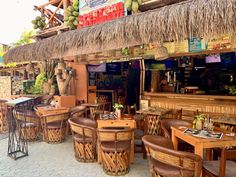 an outdoor restaurant with wicker tables and chairs, that has a tiki hut on the roof