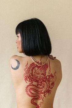 a woman with tattoos on her back is looking at the moon and dragon behind her