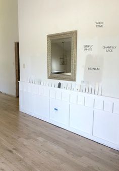 an empty room with white walls and wood flooring in the foreground is a large mirror hanging on the wall