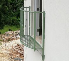 an open window on the side of a white building with green metal railings and round balconies