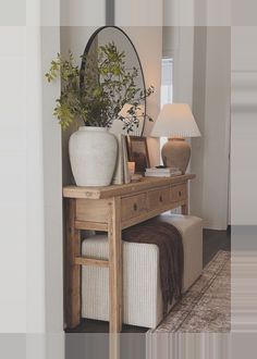 a wooden table topped with a white vase filled with flowers next to a mirror and lamp