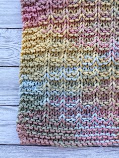 a multicolored knitted dishcloth sitting on top of a wooden table next to a spoon