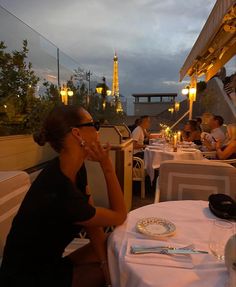 a woman sitting at a table in front of the eiffel tower during sunset