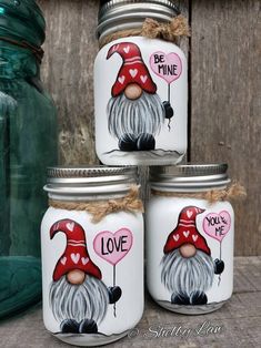 three jars with painted gnomes on them sitting next to a mason jar filled with hearts