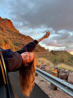 a woman leaning out the window of a car on a road with mountains in the background