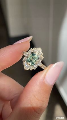 a woman's hand holding a ring with an emerald and white diamond in it