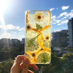 a person holding up a phone case with lemon slices and flowers on it in front of the sun