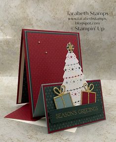 a card with a christmas tree on it and presents in the bottom corner, sitting on a table