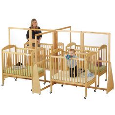 a woman standing next to two wooden cribs with toddlers in the middle