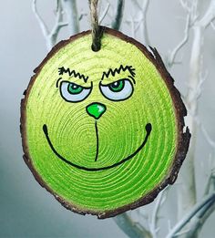 a green wooden ornament with a face drawn on it's side hanging from a tree