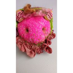 a pink and green stuffed animal with ruffles on it's head sitting on a white surface