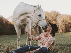 a woman sitting on the ground next to a white horse