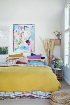 a bed with yellow sheets and pillows in a bedroom next to a painting on the wall