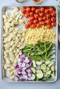 pasta salad with tomatoes, green beans, cucumbers and onions on a tray