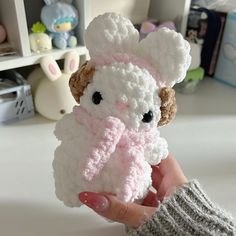 a hand holding a small crocheted white and pink stuffed animal with black eyes