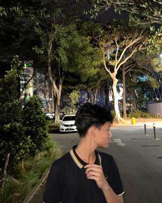 a man standing on the side of a road at night with trees and buildings in the background