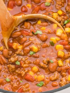 a pot filled with chili and corn next to a wooden spoon