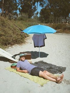 a man laying on the beach under an umbrella