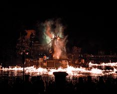 fireworks are lit up in the night sky over a large body of water with people watching