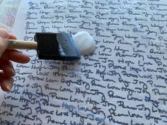 a hand holding a paint brush over a piece of paper with writing on it and an eraser next to it