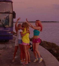 three girls are standing near the water and one is holding her hands up