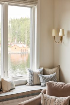 a window seat with pillows on it in front of a large window overlooking the water