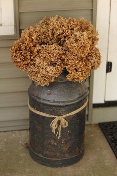 an old metal container with dried flowers in it sitting on the ground next to a door