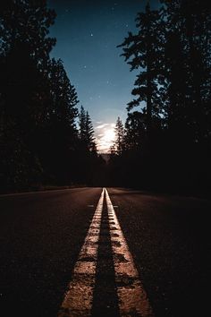 an empty road at night with the moon in the sky and trees on either side