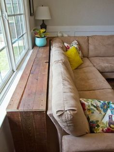 a couch sitting in front of a window next to a wooden table with pillows on it