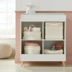 a baby's nursery room with pink walls and white shelves filled with baskets, toys and stuffed animals