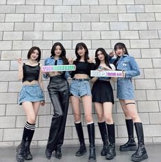 four girls are holding up signs in front of a brick wall and posing for the camera