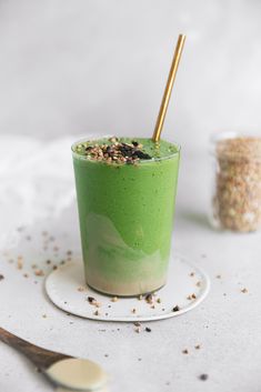 a green smoothie in a glass with gold straws on the rim and sprinkles around it