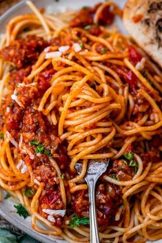 spaghetti with meat sauce and parmesan cheese on a white plate next to bread