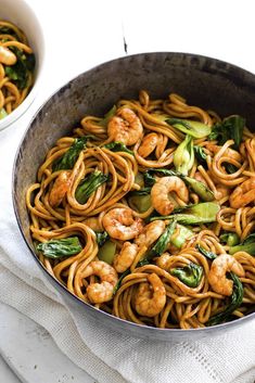 two pans filled with noodles and shrimp on top of a white cloth next to each other