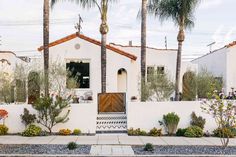 a white house with palm trees in front of it and flowers on the side walk