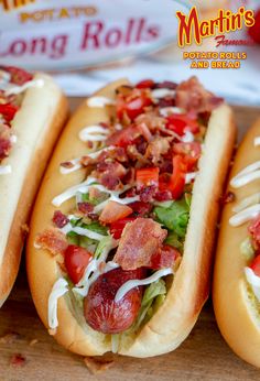 three hot dogs with toppings on them sitting on a cutting board