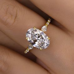 a woman's hand with a diamond ring on top of her finger and an oval shaped diamond in the middle